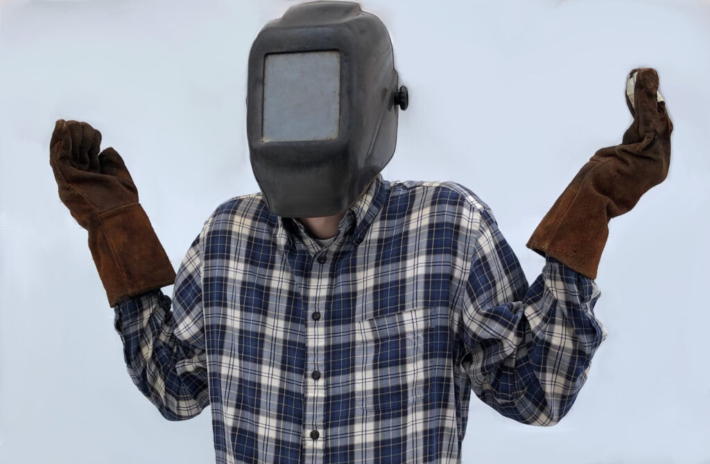 Man wearing welding hood lifting arms and shrugging shoulders